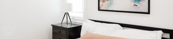 Above bed wall art featuring a framed coastal photograph over white pillows