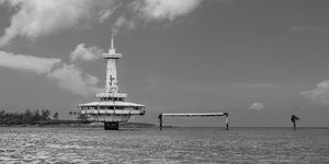 Fotografia panoramica monocromatica di una torre al largo delle Bahamas e di una piattaforma in rovina.