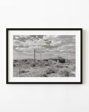 Abandoned buildings in Currie, Nevada, among desert scrub beneath a cloud-filled sky.