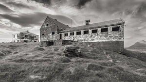 Weathered Icelandic farm walls and a stripped vehicle beneath a cloudy sky.