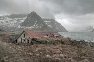 Weathered timber boathouse on a rocky Norwegian shore beneath low cloud.