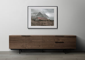 Muted colour photograph of an abandoned Lofoten boathouse and snow-streaked mountains.