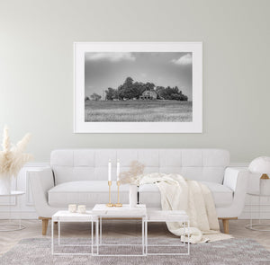 Old brick farmhouse and surrounding trees beneath scattered clouds in monochrome