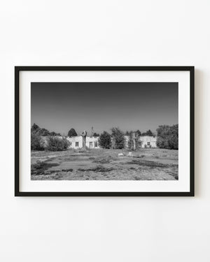 Abandoned roadside motel behind two cut tree trunks in black and white