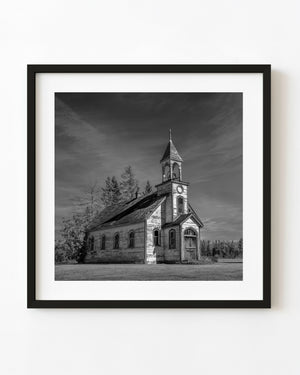 Abandoned Saskatchewan wooden church beneath a streaked sky in black and white