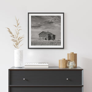 Black and white prairie landscape with a weathered building and low open horizon.