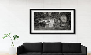 Black and white photograph of an overgrown café with boarded lower windows and a long roofline.