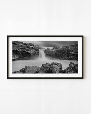 Aldeyjarfoss waterfall dropping between dark basalt columns and rough foreground rocks in Iceland.