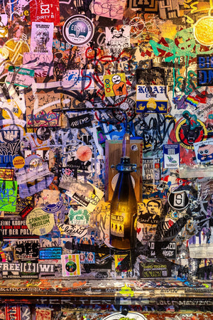 Lámpara de botella brillando contra un denso collage de pegatinas dentro de un pub de Ámsterdam.