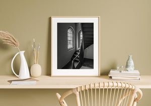 Monochrome photograph of a timber stairwell and gridded arched windows.