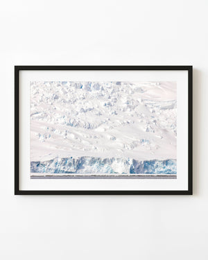 Blue Antarctic ice cliffs below a broad snow-covered slope and above dark water.