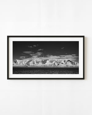 Panoramic black and white Antarctic snow mountains above a dark ocean.
