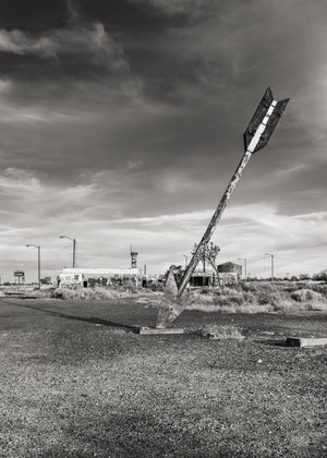 Sculpture de flèche penchée à côté de bâtiments bas en bordure de route sous un ciel nuageux de l'Arizona.