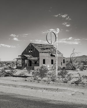 Weathered Route 66 building with exposed roof timbers and an empty round roadside sign.