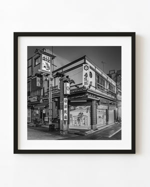 A shuttered corner restaurant in Asakusa, Tokyo, with painted panels and tall signs in black and white.
