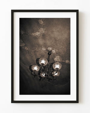 An antique chandelier hangs beneath a faded floral ceiling in warm monochrome in Barcelona.