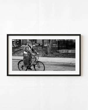 A bearded cyclist rides through Toronto in black and white with open street ahead.