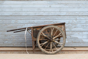 Large spoked wheel and rusty tray beside peeling blue paint