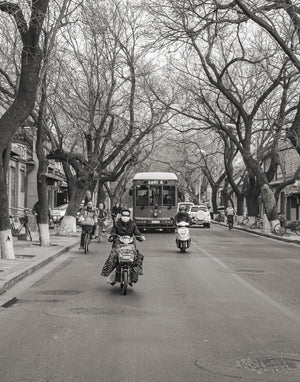 Des scooters et des cyclistes de Pékin s'approchant sous des branches sans feuilles entrelacées
