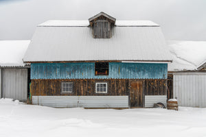 Colour winter photograph of a blue and brown wooden barn surrounded by snow.