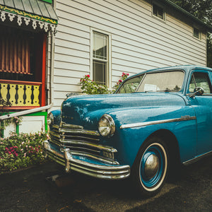 Square colour photograph of a blue classic Plymouth with chrome grille and whitewall tyre.