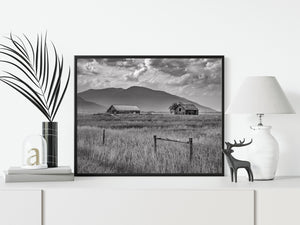 Landschaft in British Columbia mit verwitterten Holzgebäuden und einer wolkigen Bergkulisse.