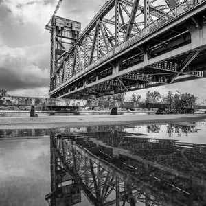 Steel bridge trusses and their reflection beneath clouds in Hamilton, Ontario.