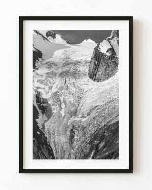 Black and white photograph of a Canadian mountain glacier beside a sheer dark rock face.
