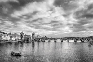 Los arcos del puente de piedra cruzan el río debajo de las históricas torres de Praga y un cielo texturizado.