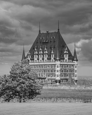 Steile Dächer und Fensterreihen definieren Chateau Frontenac über belaubten Bäumen im Vordergrund.