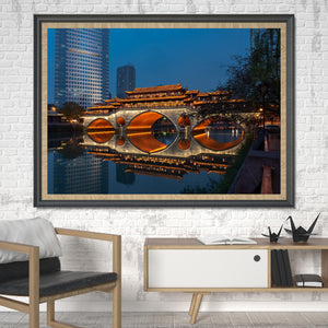 Chengdu’s illuminated Anshun Bridge sits between shadowed trees and modern towers beside calm water.