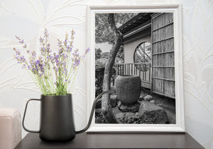 Black and white garden scene with a stone basin, circular window and sloping roof edge.