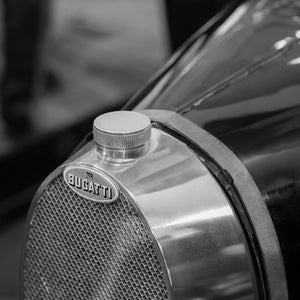 A Bugatti badge sits beneath a round radiator cap in a monochrome classic-car detail photograph.