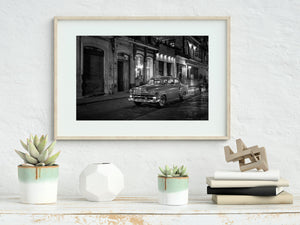 Bright chrome on a Havana taxi contrasts with shadowed walls in a night street photograph.