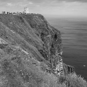 An Irish cliff-top tower overlooks steep rock faces and open Atlantic water in monochrome.