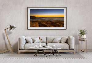 A low golden horizon glows beyond layered coastal rocks and still pools in Australia.