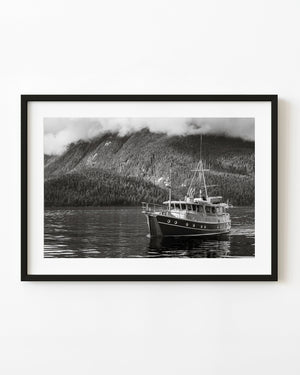 Black and white photograph of a coastal boat on British Columbia water beneath forested mountains and low fog.