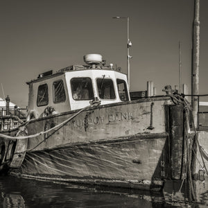 A worn wooden fishing boat sits beside harbour posts with its cabin above the bow.