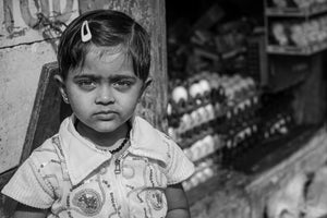 A girl with hair clips looks toward the camera with shop goods behind her.