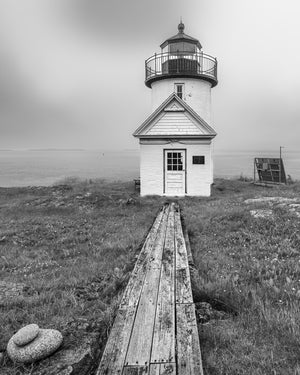 Weathered boards cross low coastal vegetation towards a small white lighthouse on Curtis Island.