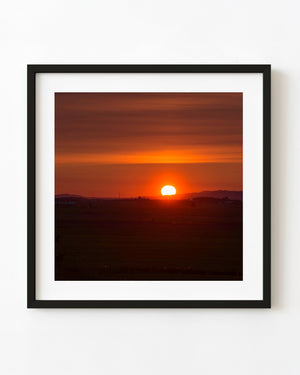 A bright sun rises above dark rural Quebec fields beneath a deep red and orange sky.
