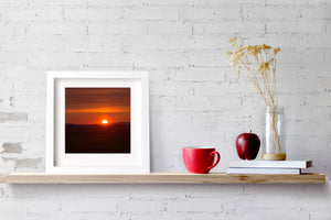 Deep red tones fill the sky as the sun appears just above a dark line of hills.