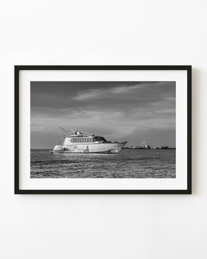 Derelict yacht anchored in Key West beneath streaked clouds, black and white photograph.