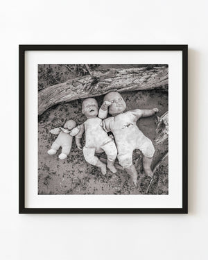 Three discarded dolls beneath weathered timber in the Southwest, black and white photograph.