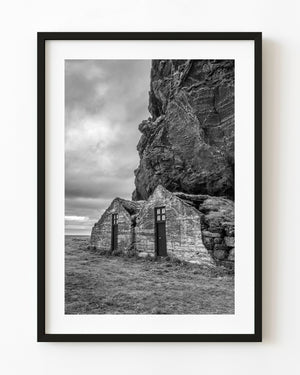 Drangshlid turf houses beneath a rugged cliff in black and white