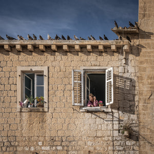 Dubrovnik-Steinfassade mit einer Frau an einem offenen Fenster und einer Katze in der Nähe