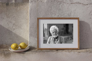Indian man with loose white hair and tilted glasses in a horizontal monochrome photograph