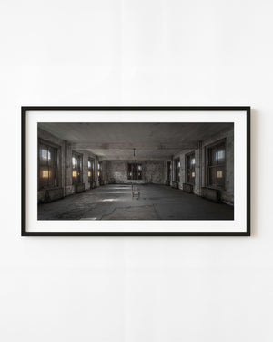 A solitary chair between rows of tall windows in Ellis Island’s abandoned hospital ward.