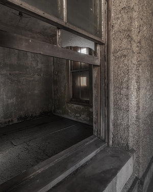 Sepia photograph looking through a broken window into Ellis Island’s abandoned hospital.