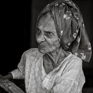Indian woman in a headscarf looks to the side against a dark background.